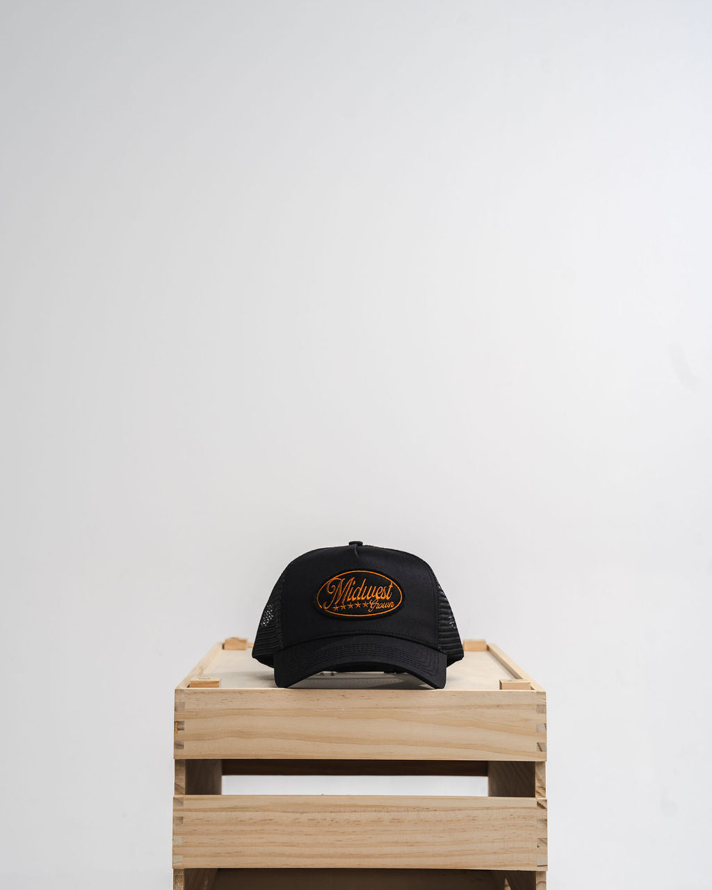 Black cap with gold Midwest Grown logo on a wooden crate against a white background