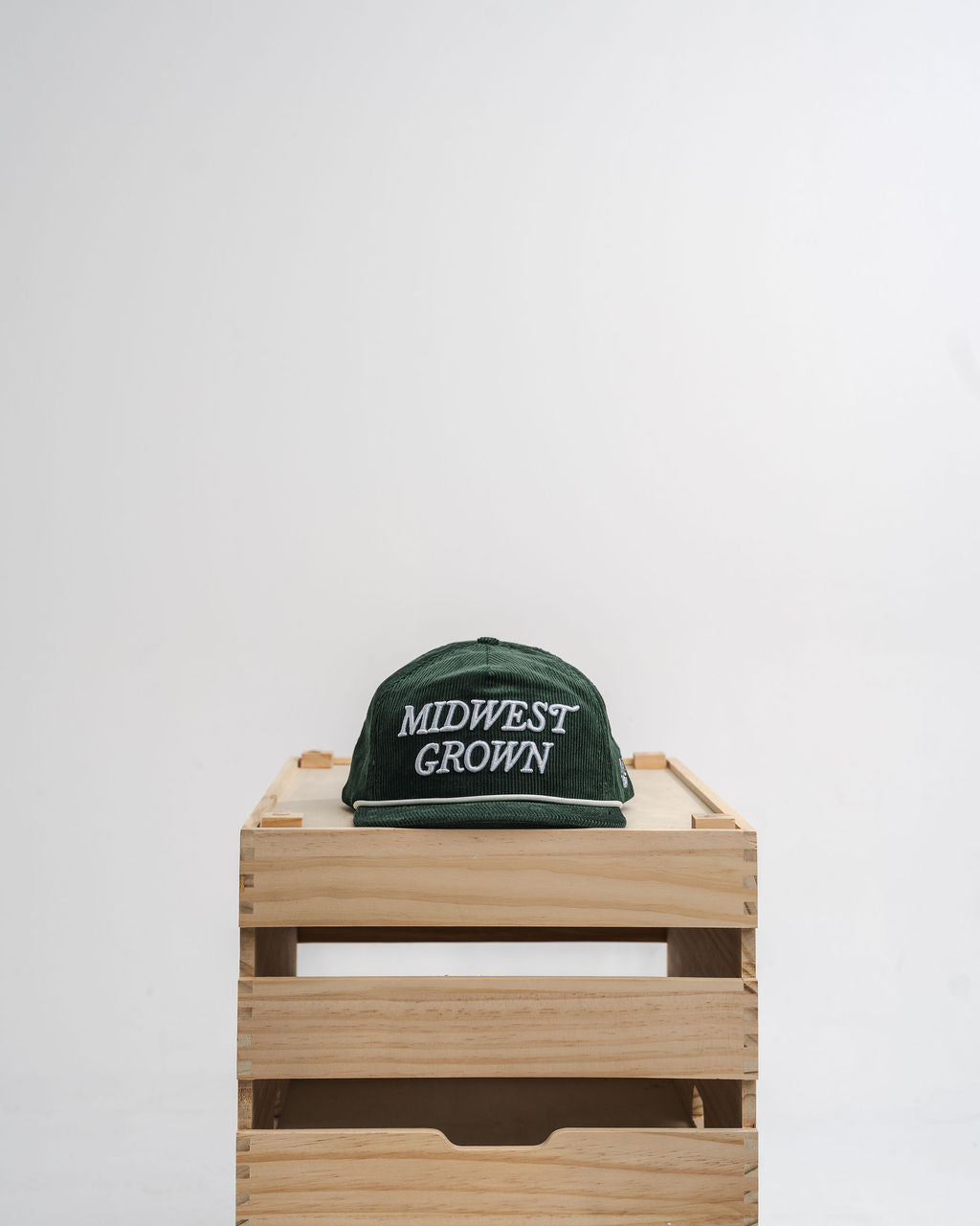 Green hat with 'Midwest Grown' text on a wooden crate against a white background