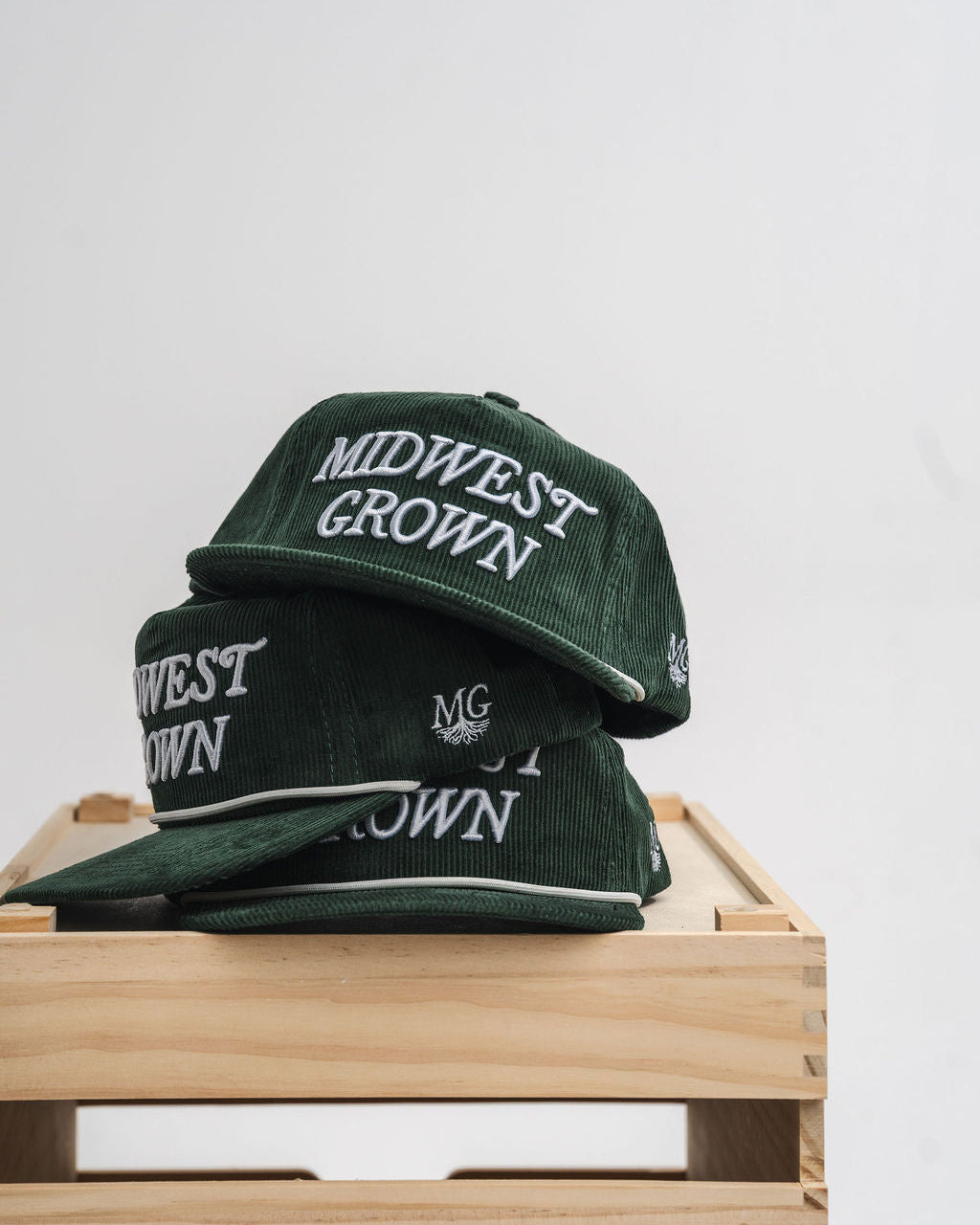 Green hats with 'Midwest Grown' text on a wooden surface