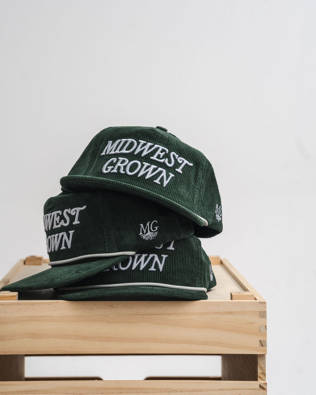 Green hats with 'Midwest Grown' text on a wooden surface
