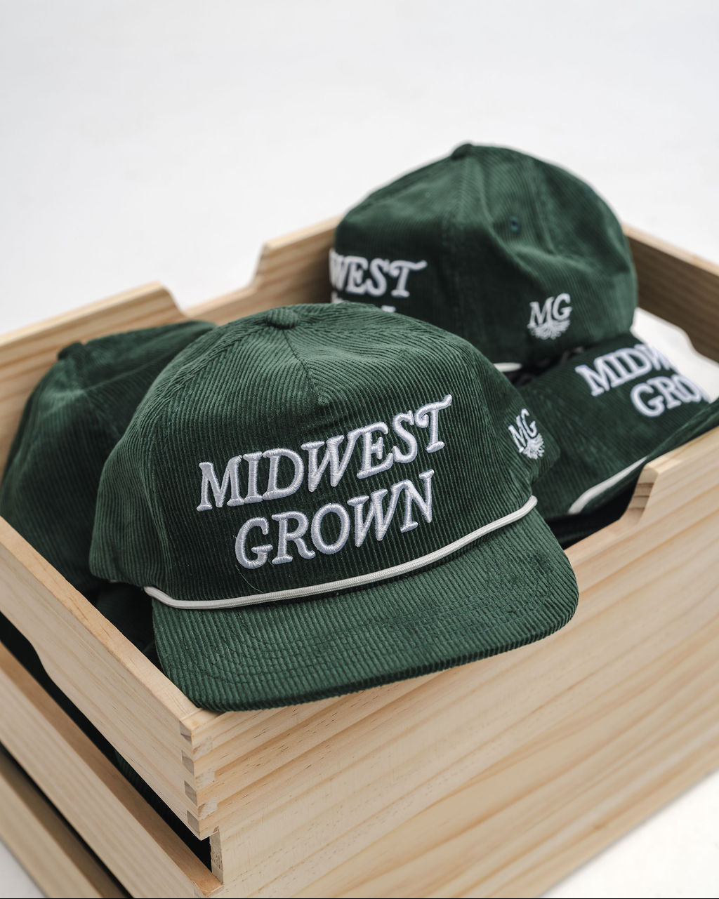 Green caps with 'Midwest Grown' text in a wooden crate on a white background