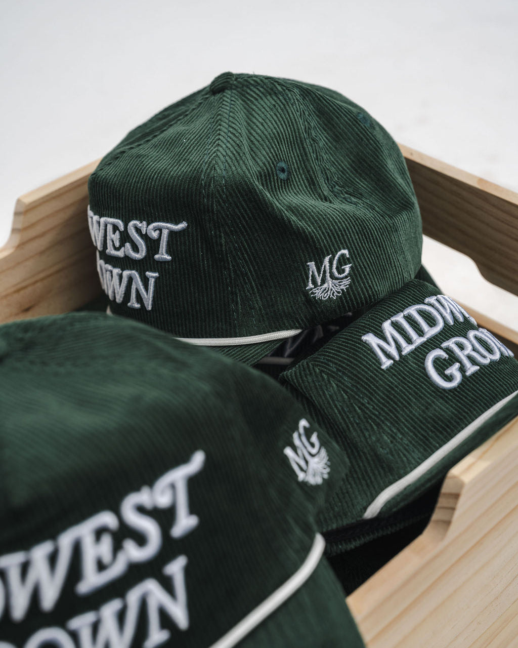 Green caps with 'West Grown' and 'Midwest Grown' text on a wooden surface.