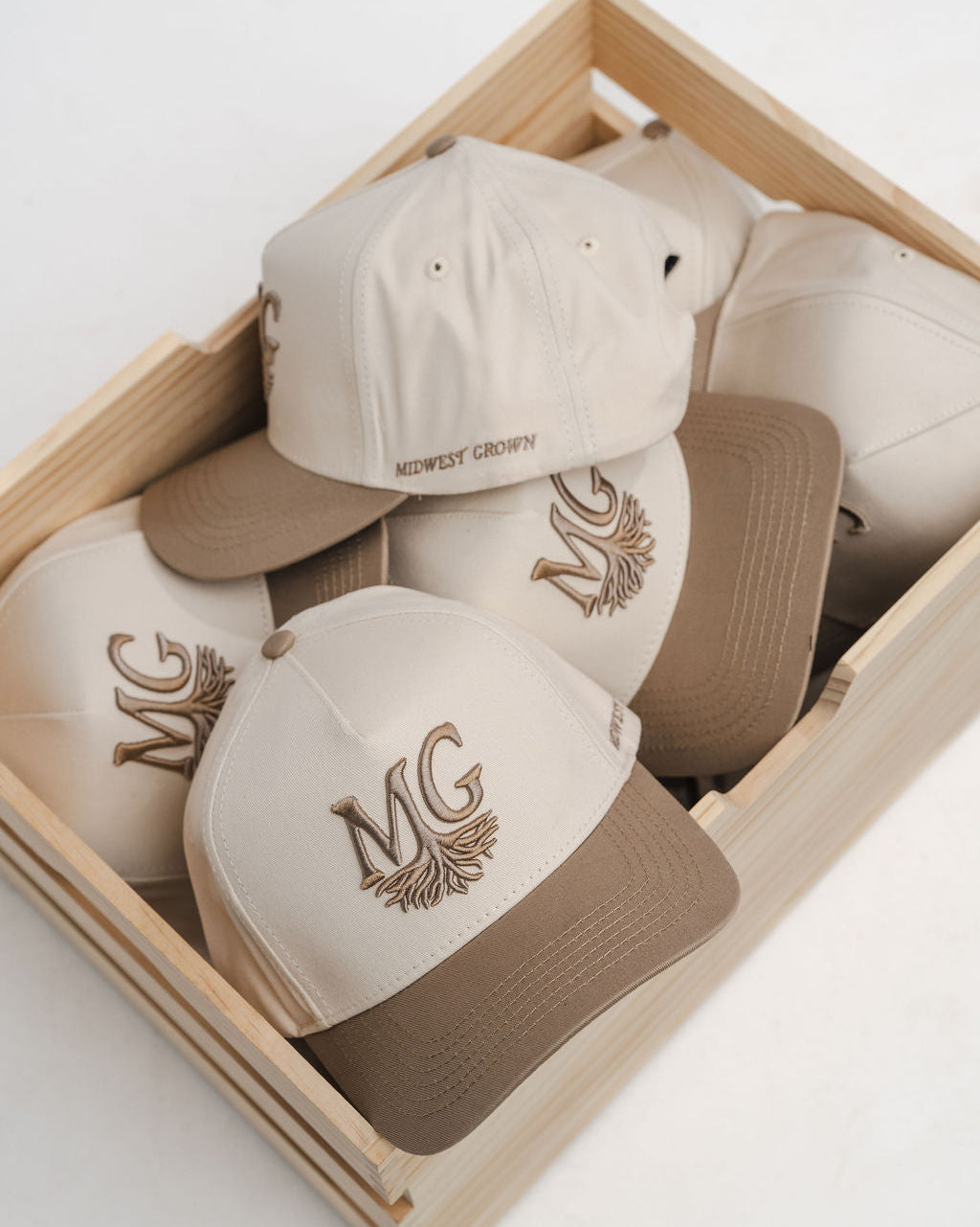 Set of beige and brown caps with 'Midwest Grown' logo in a wooden box on a light background