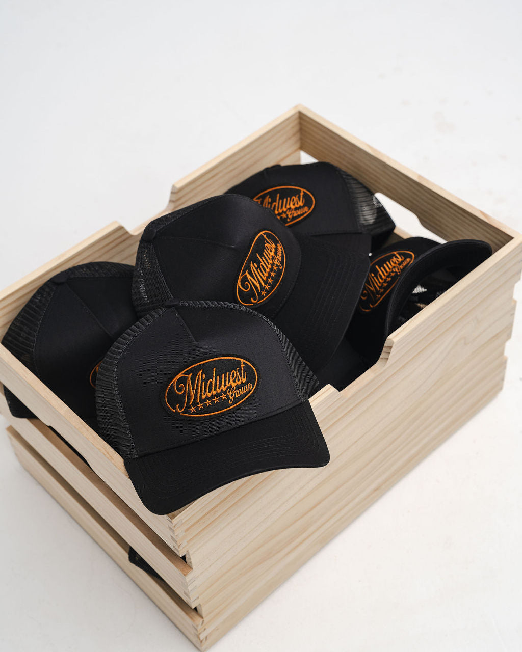 Black Midwest Grown caps with a logo in a wooden crate on a white background