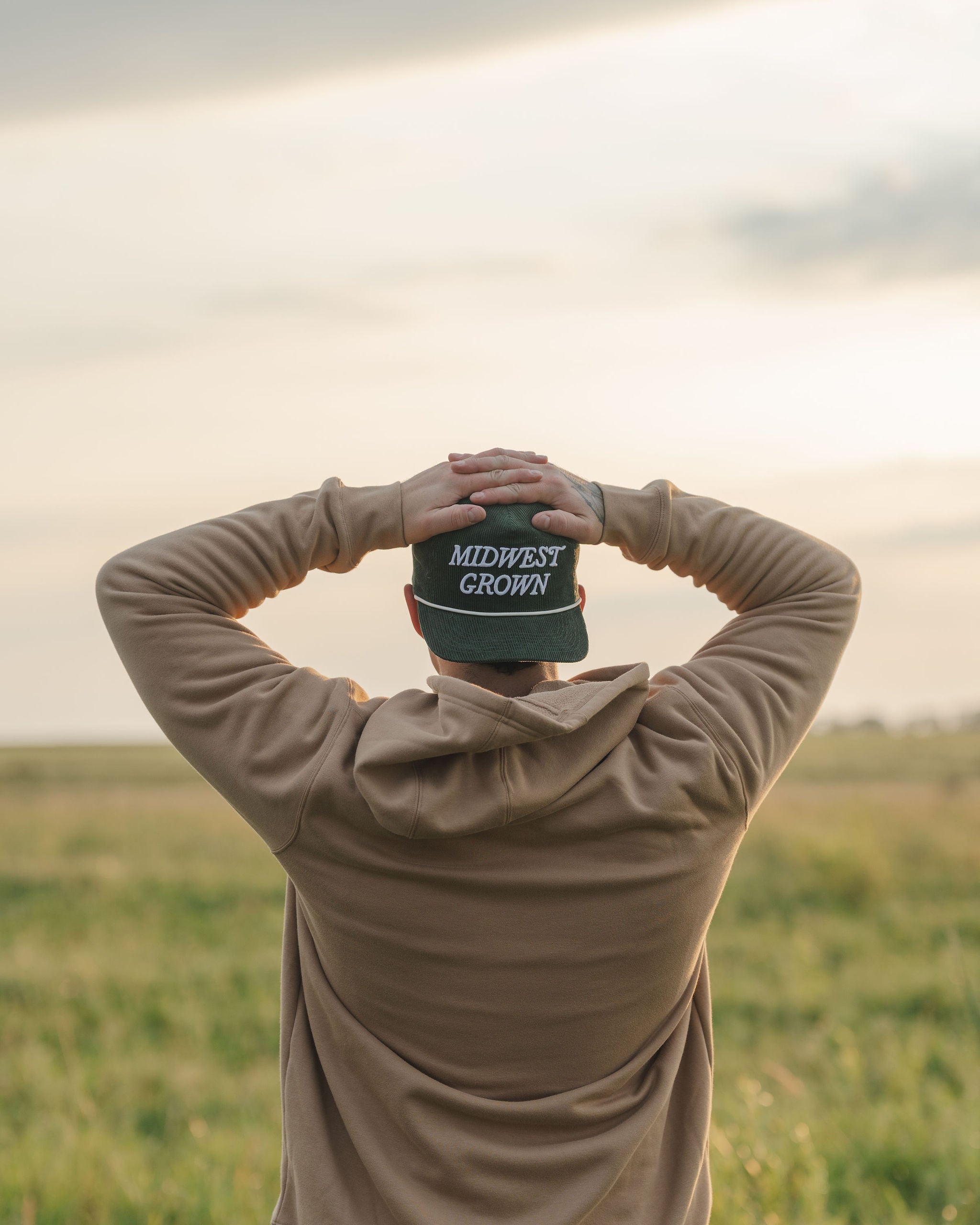 Person holding a cap with 'Midwest Crown' text in a field