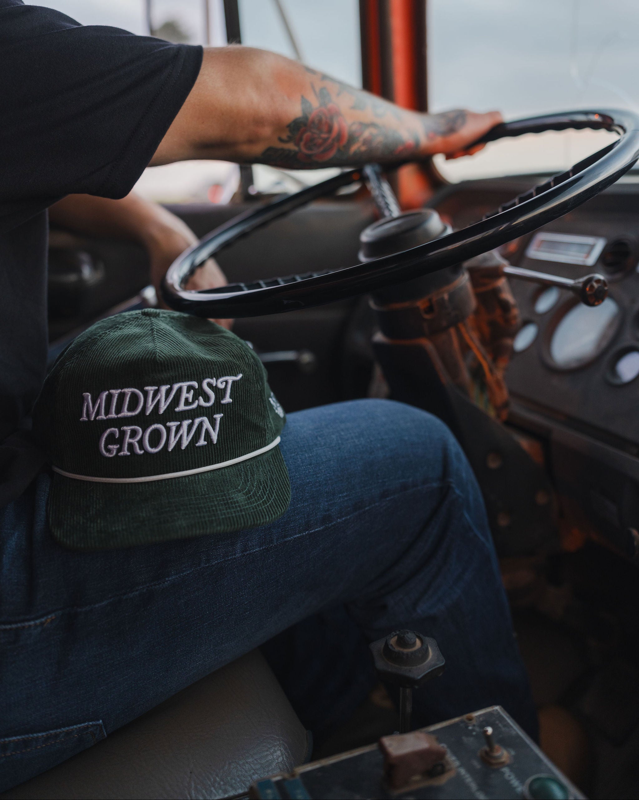 Person sitting inside a vehicle with a 'Midwest Grown' cap on their lap.