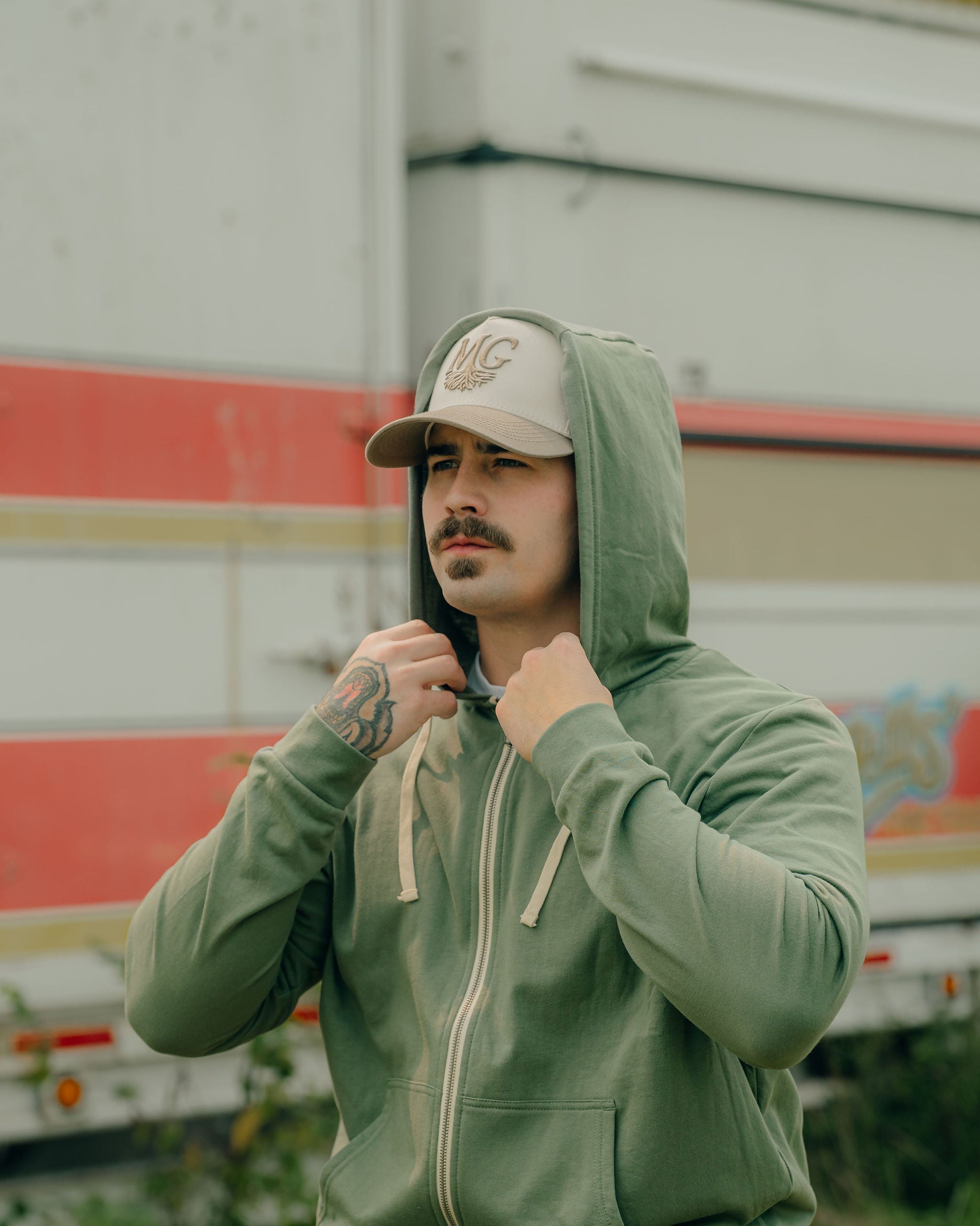 Man wearing a green hoodie and beige Midwest Grown cap in front of a colorful truck.