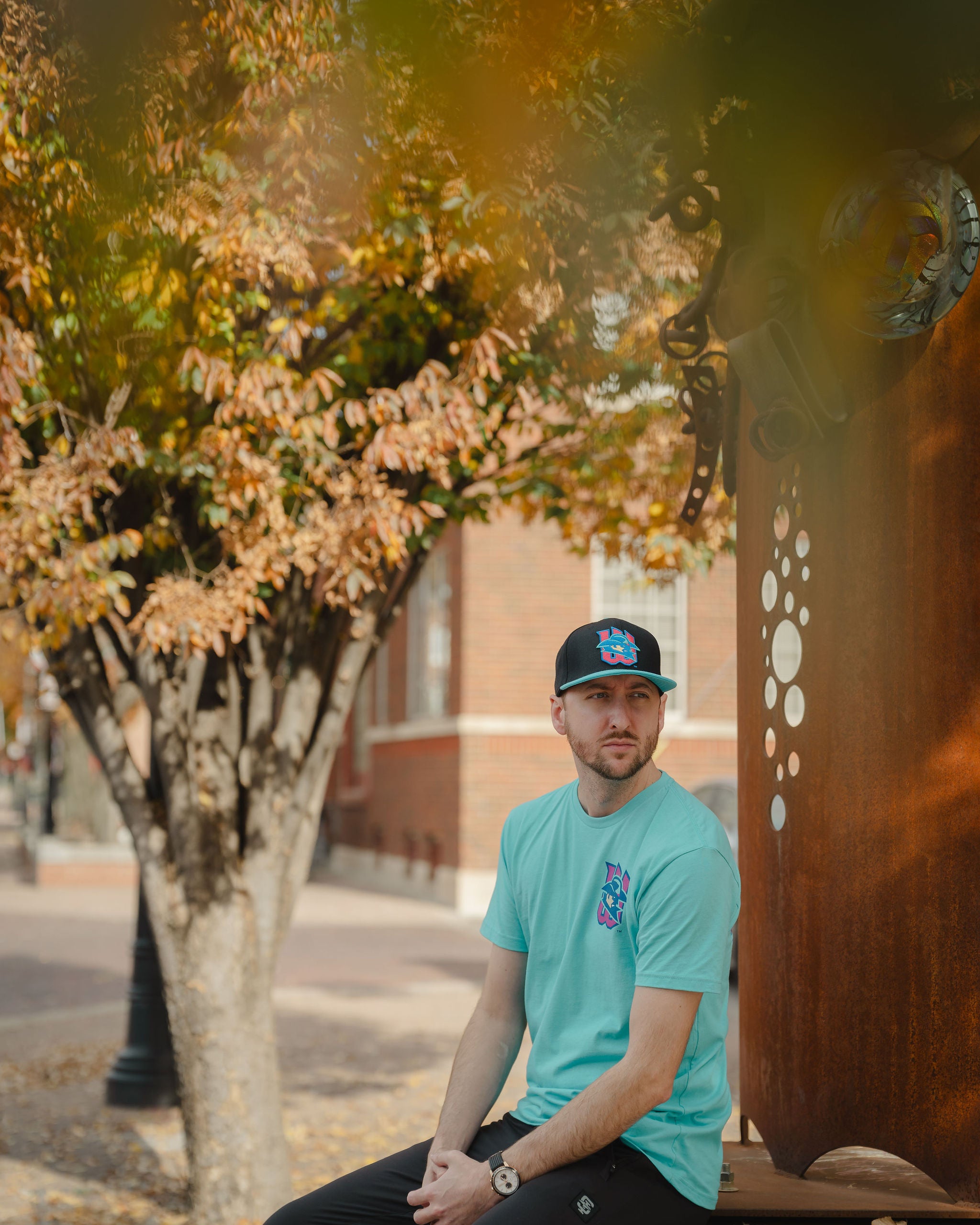 Man sitting on a bench with a tree and building in the background