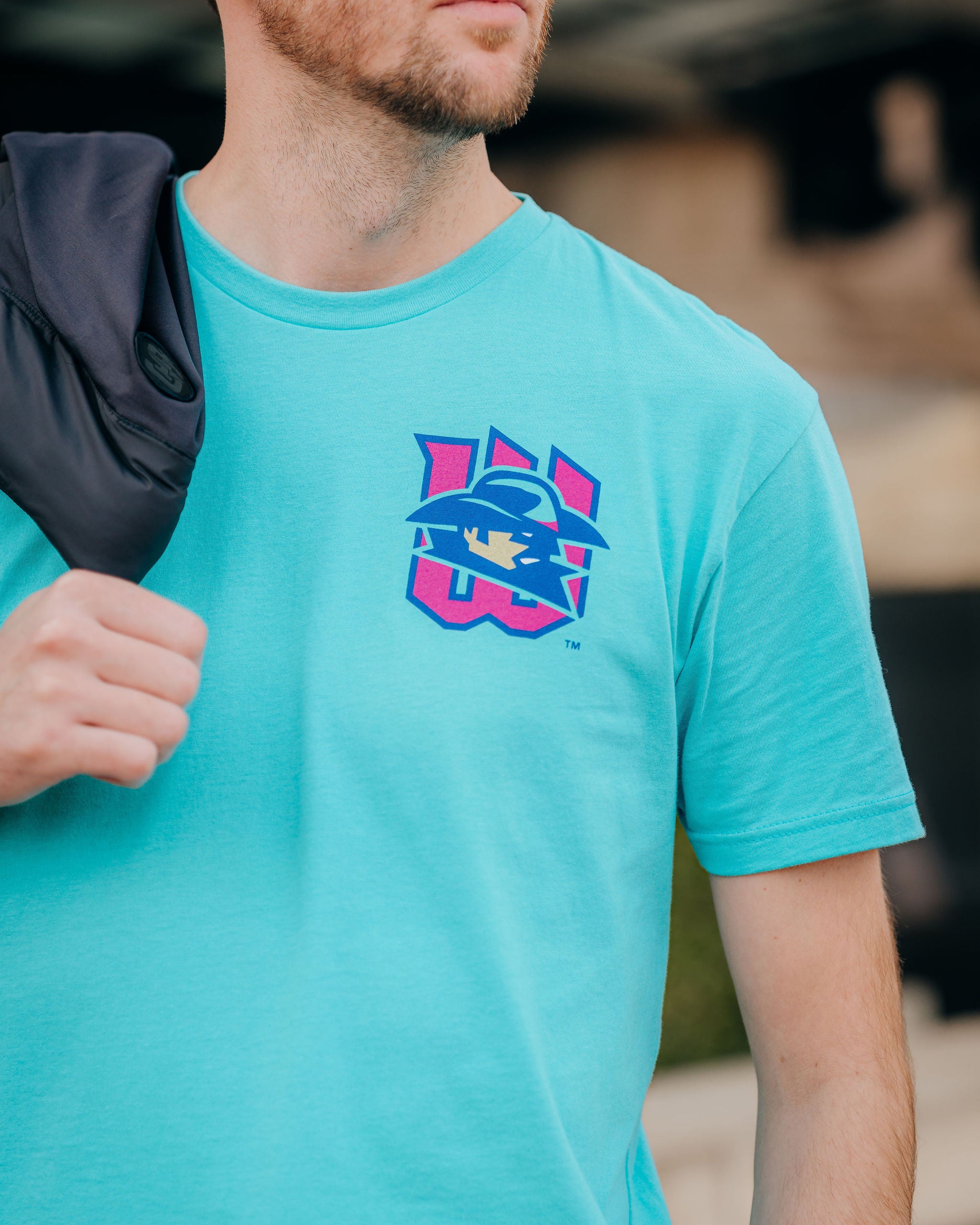 Person wearing a turquoise t-shirt with a logo, standing outdoors.