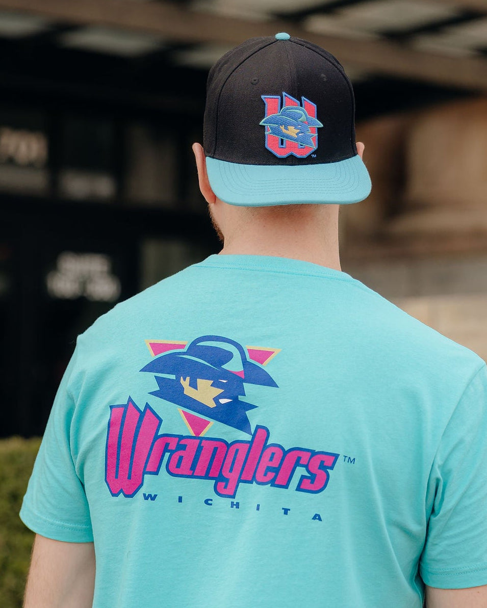 Person wearing a turquoise 'Wranglers' t-shirt and black cap outdoors.