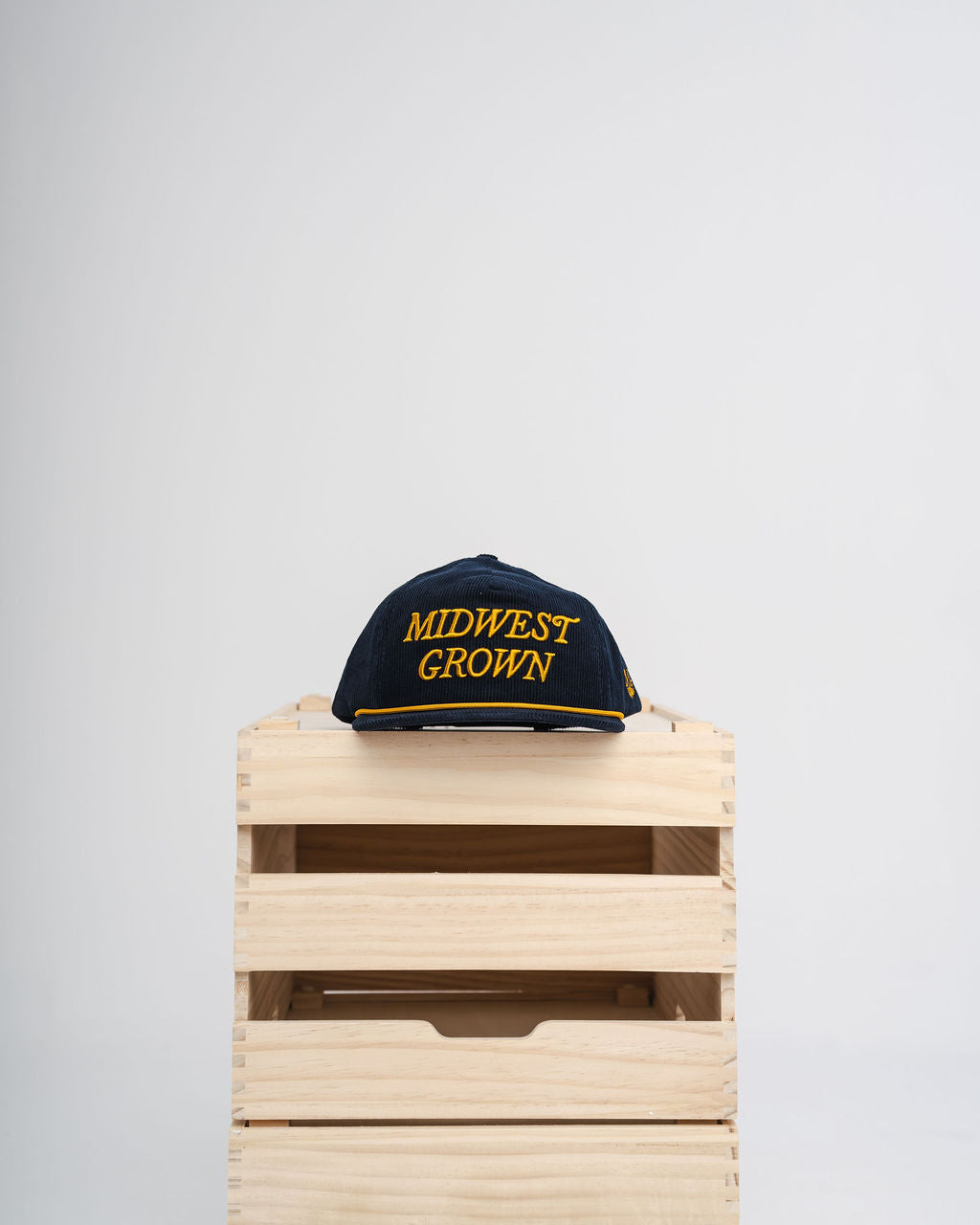 Cap with 'Midwest Grown' text on a wooden crate against a light gray background