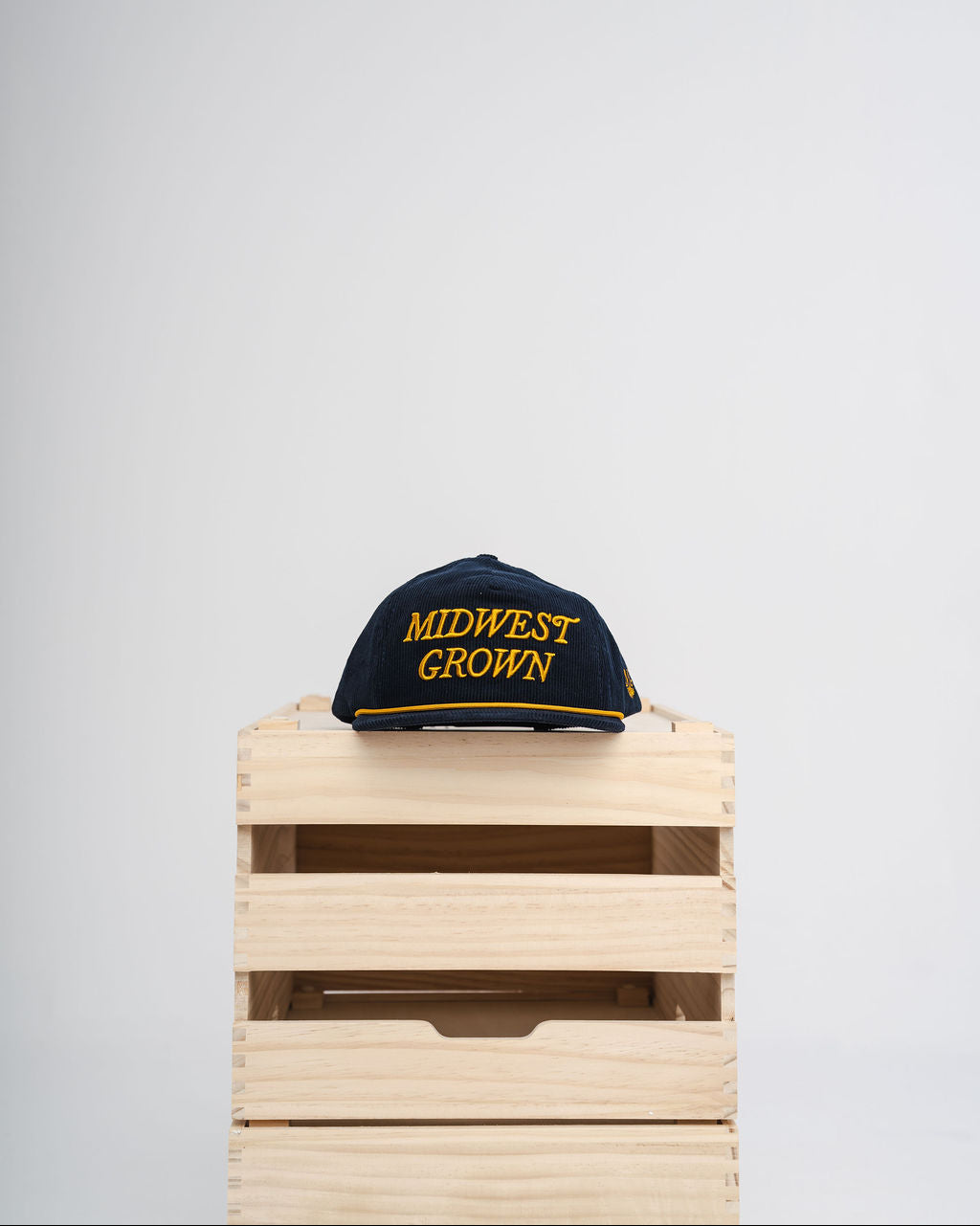 Cap with 'Midwest Grown' text on a wooden crate against a light gray background