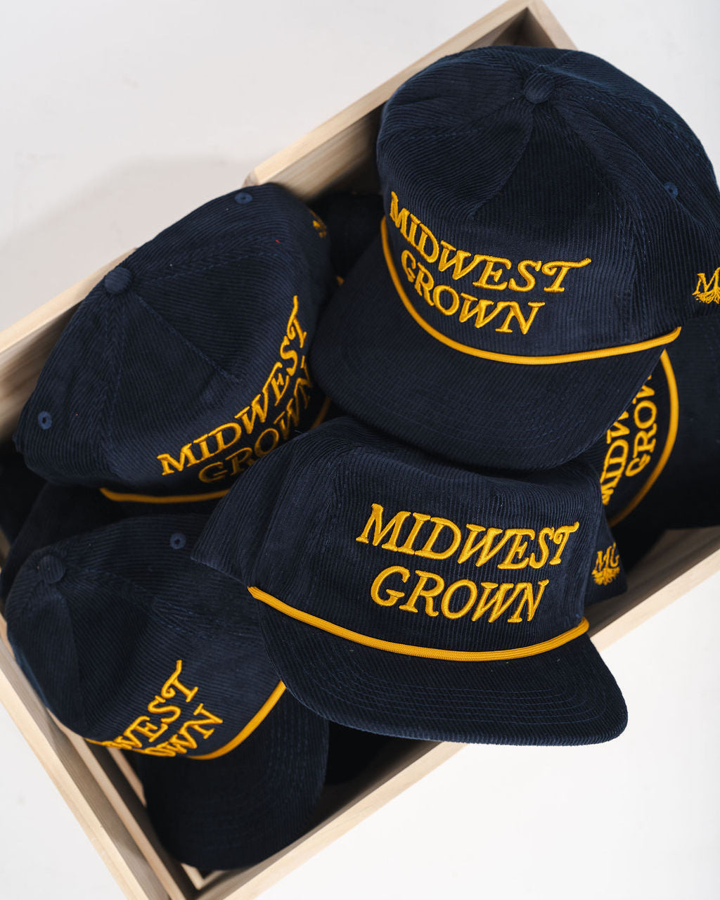 Box containing navy blue caps with 'Midwest Grown' text on a white background