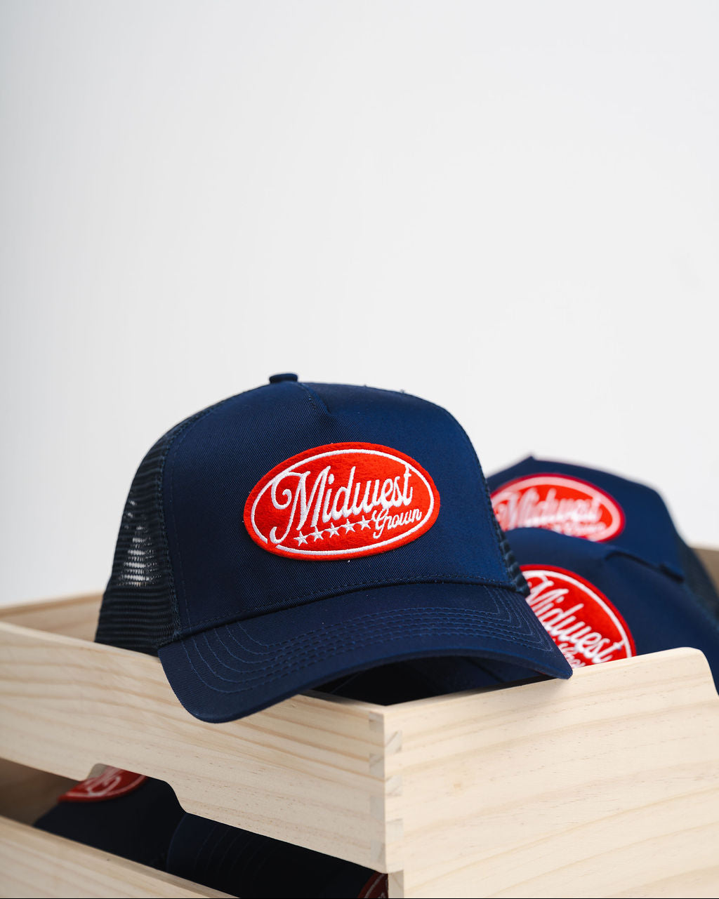 Two navy blue Midwest Grown hats with a red logo on a wooden surface
