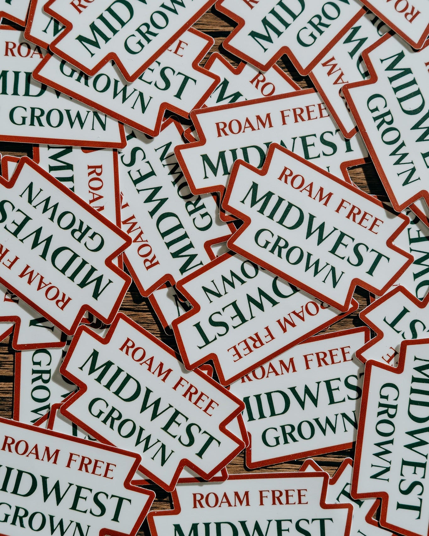 Stack of 'Midwest Grown' and 'Roam Free' stickers on a wooden surface.