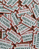 Stack of 'Midwest Grown' and 'Roam Free' stickers on a wooden surface.