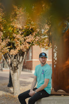 Man sitting on a bench with a tree and building in the background
