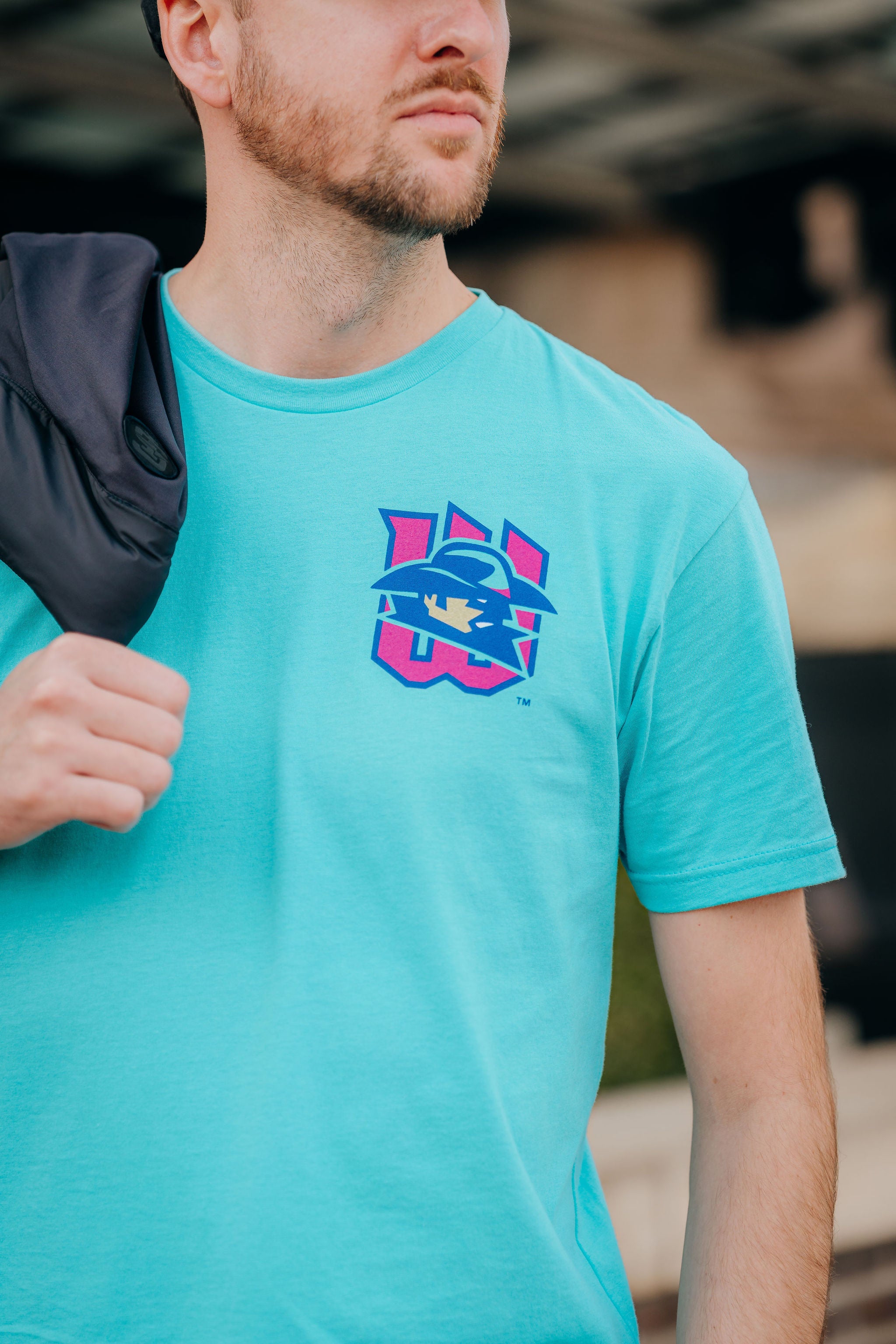 Person wearing a turquoise t-shirt with a logo, standing outdoors.