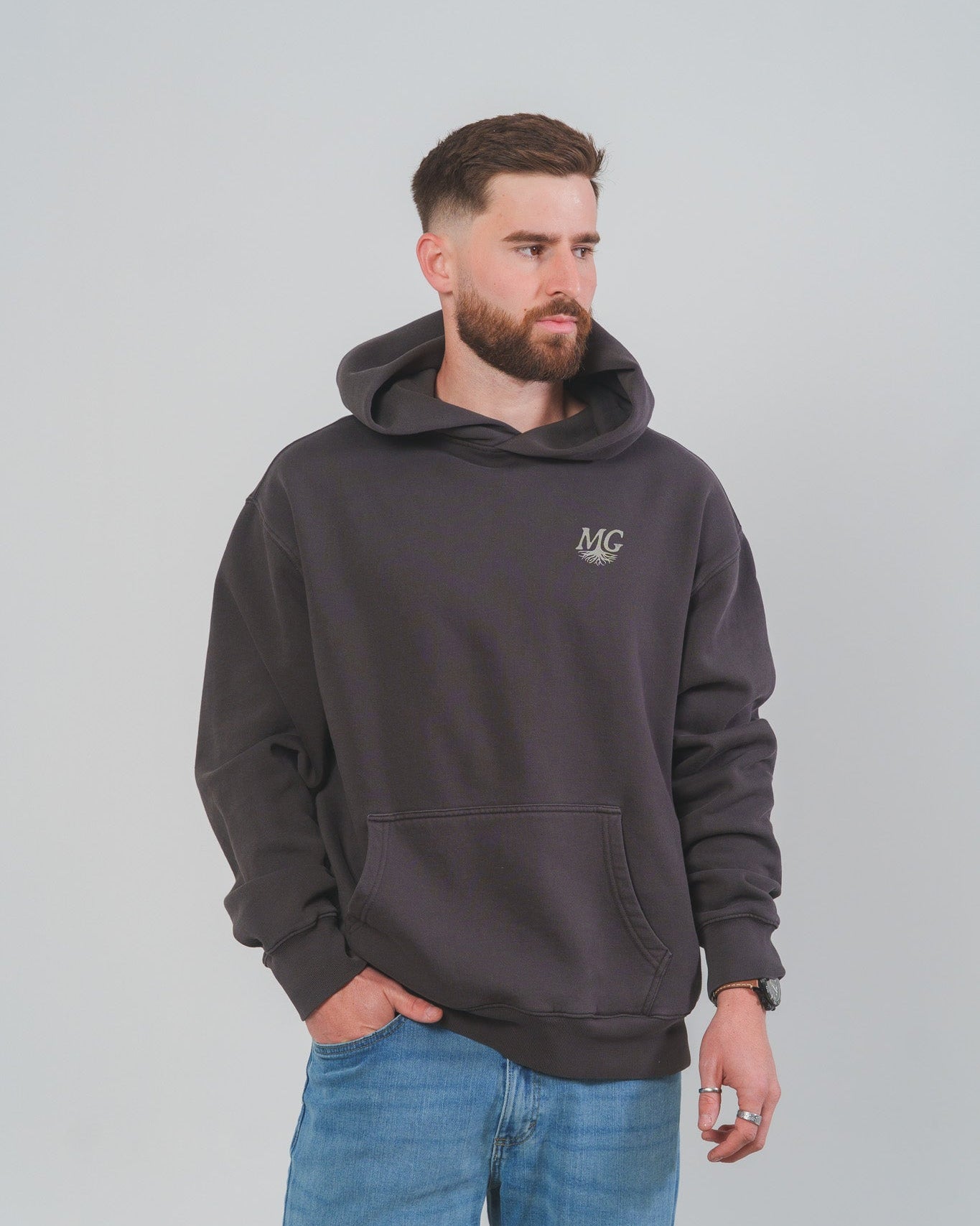 Man wearing a dark gray Midwest Grown hoodie with a logo on a plain background