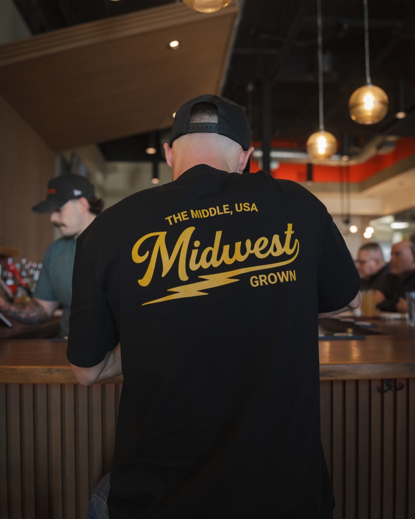Person wearing a black t-shirt with 'Midwest Grown' text in a casual setting