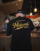 Person wearing a black t-shirt with 'Midwest Grown' text in a casual setting