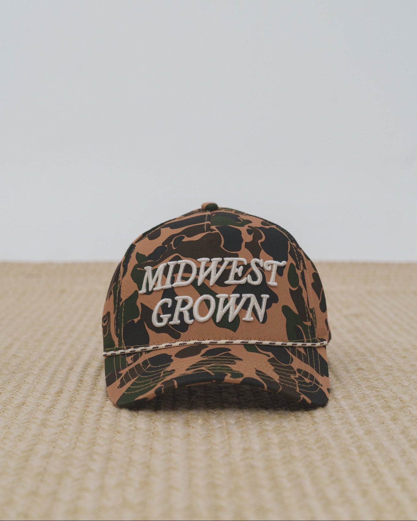 Duck Camouflage-patterned cap with 'Midwest Grown' text on a textured surface.