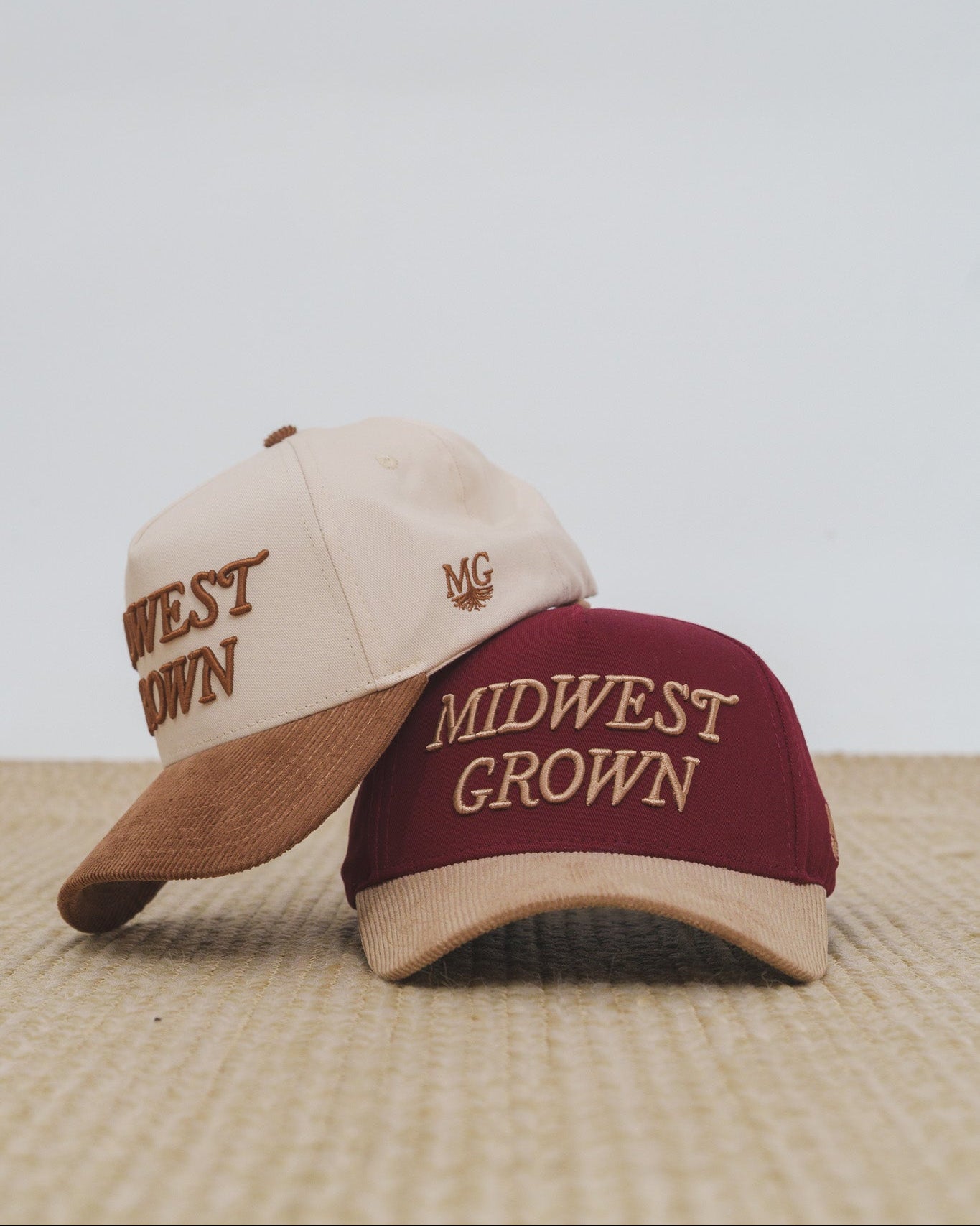 Two baseball caps with 'Midwest Grown' text on a textured surface and light background