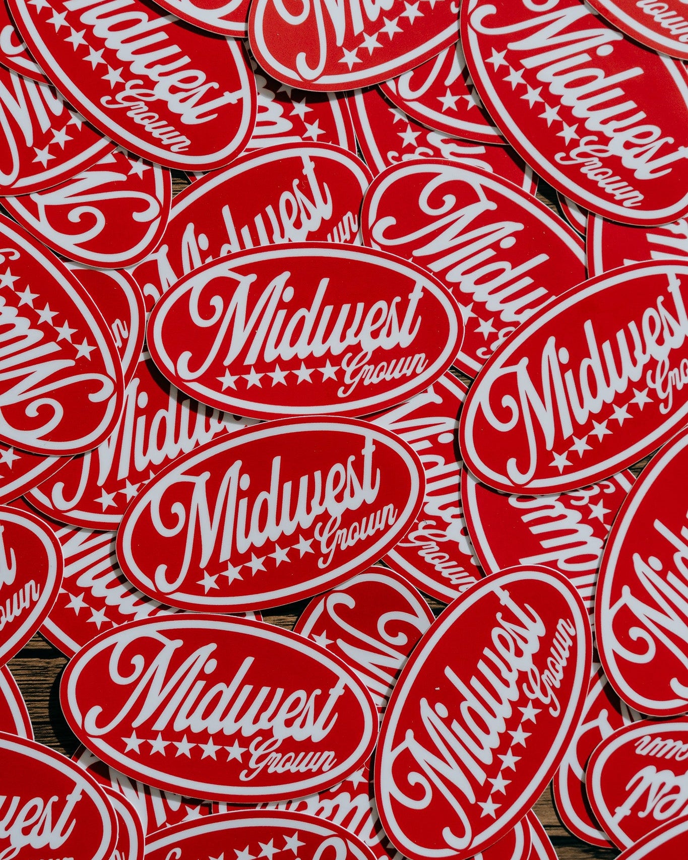 Stack of red and white stickers with 'Midwest Grown' text on a wooden surface.
