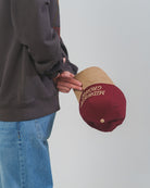 Person holding a maroon and beige Midwest Grown hat.