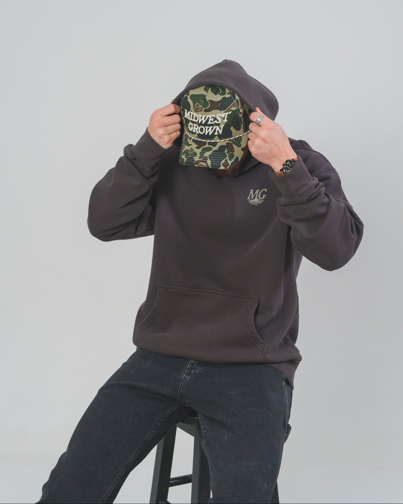 Person wearing a dark Midwest Grown hoodie with a camouflage pattern Midwest Grown Hat on.